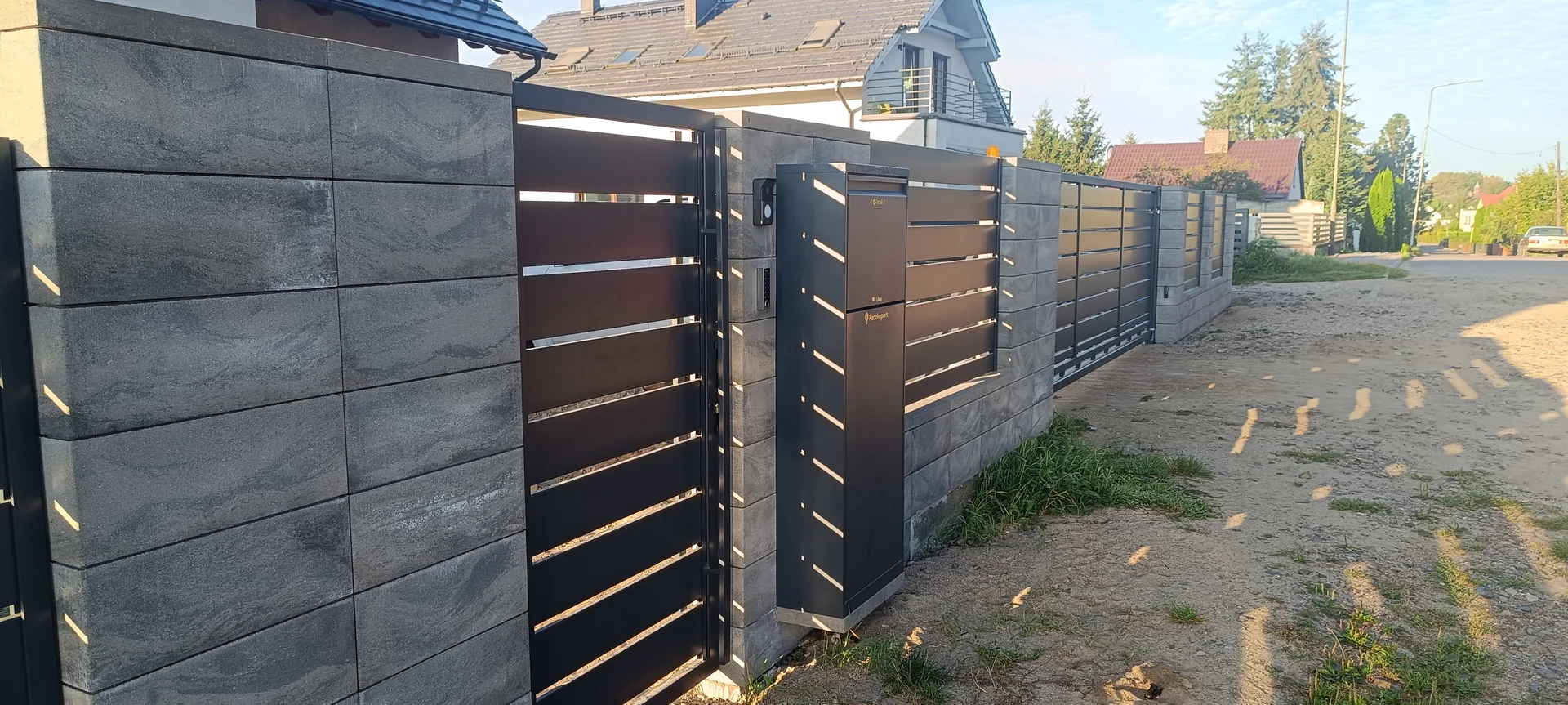 Brama wjazdowa z przęsłami metalowymi, zintegrowana z ogrodzeniem betonowym