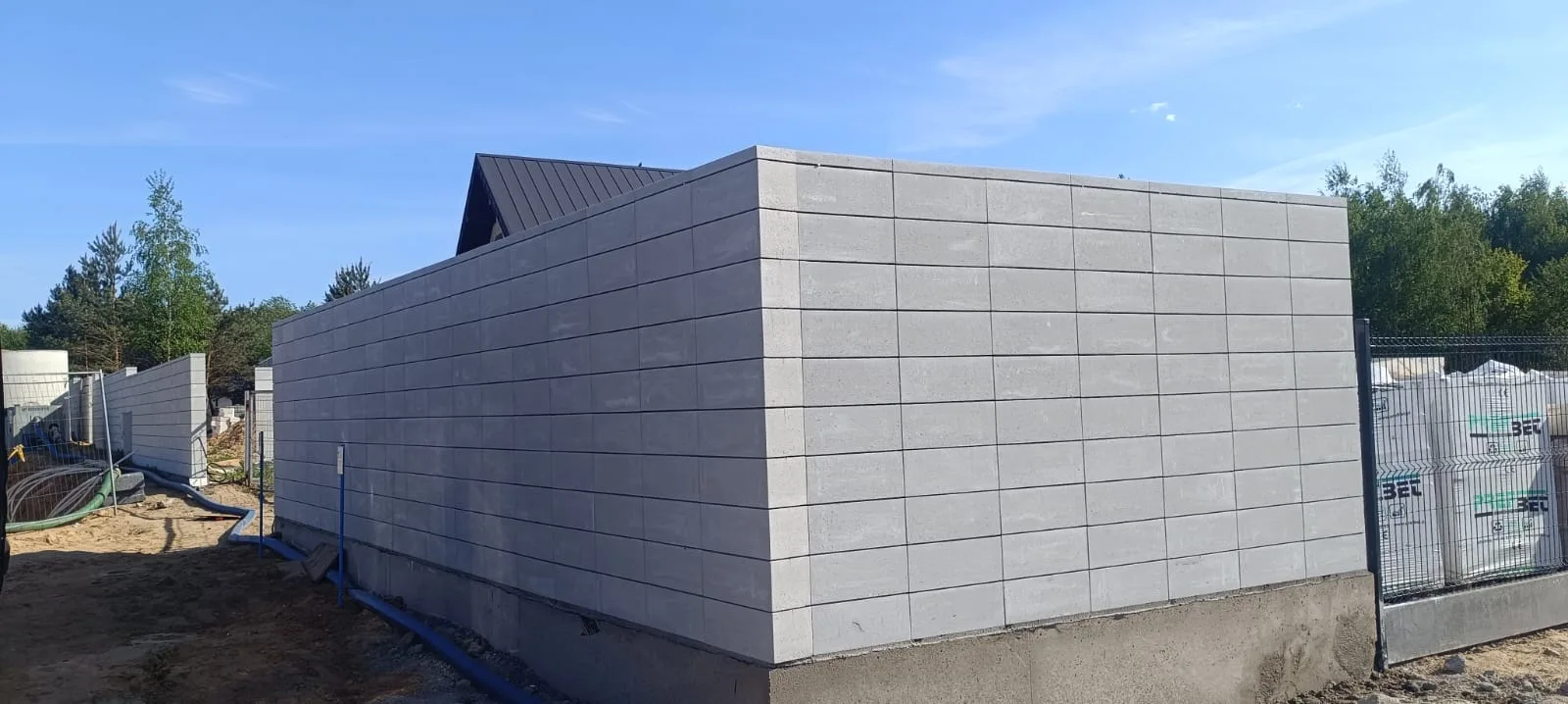 Panele betonowe ogrodzenia w kolorze szarym montowane wokół budynku z metalową bramą wjazdową