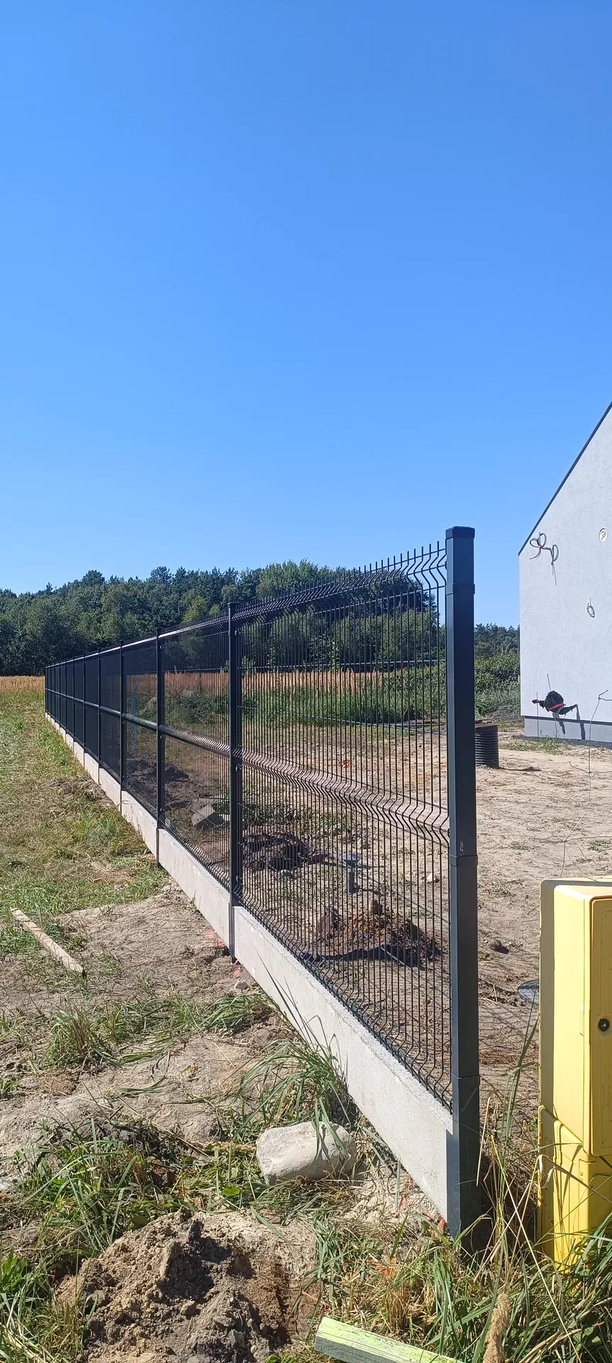 Ogrodzenie siatkowe z czarnymi słupkami metalowymi i białą podmurówką, perspektywa wzdłuż linii