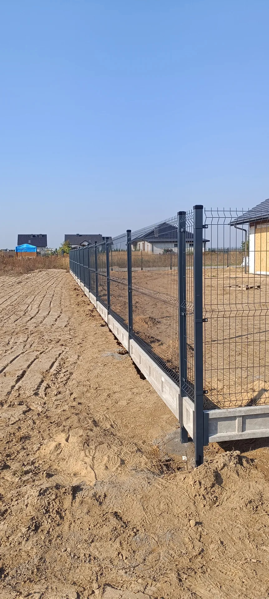 Ogrodzenie siatkowe z czarnymi słupkami metalowymi na białej podmurówce betonowej