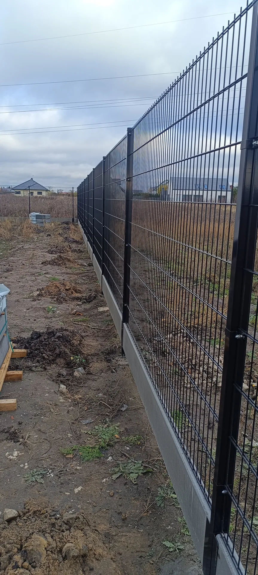 Ogrodzenia siatkowe z czarnymi słupkami metalowymi na betonowej podmurówce
