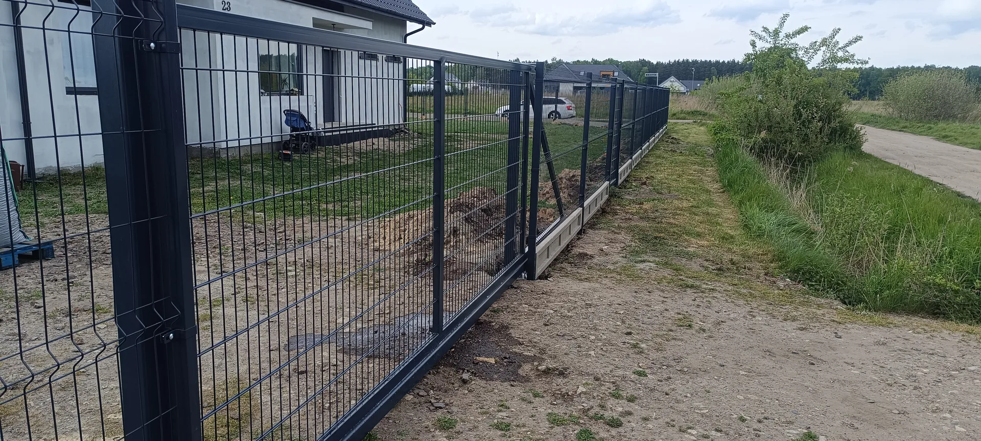 Czarne ogrodzenie siatkowe z bramą wjazdową, metalowymi słupkami i podmurówką