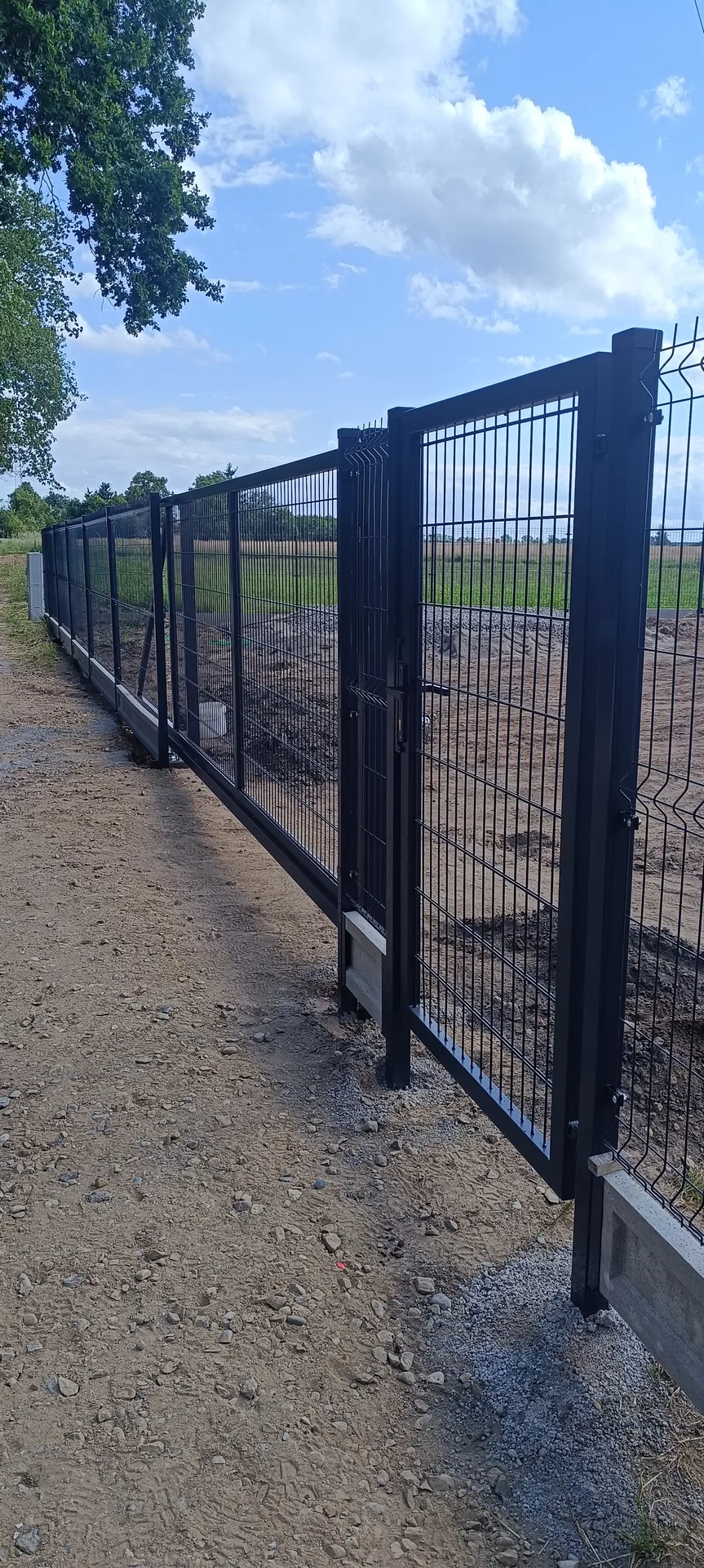 Ogrodzenia metalowe z czarnymi słupkami i metalową siatką, wzdłuż terenu otwartego