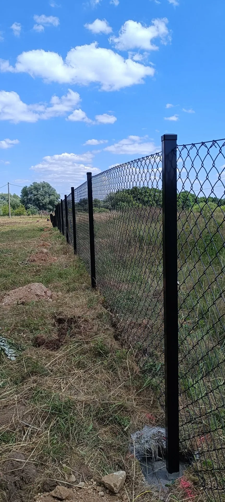 Czarne słupki metalowe z siatką ogrodzeniową montowane na terenie otwartym