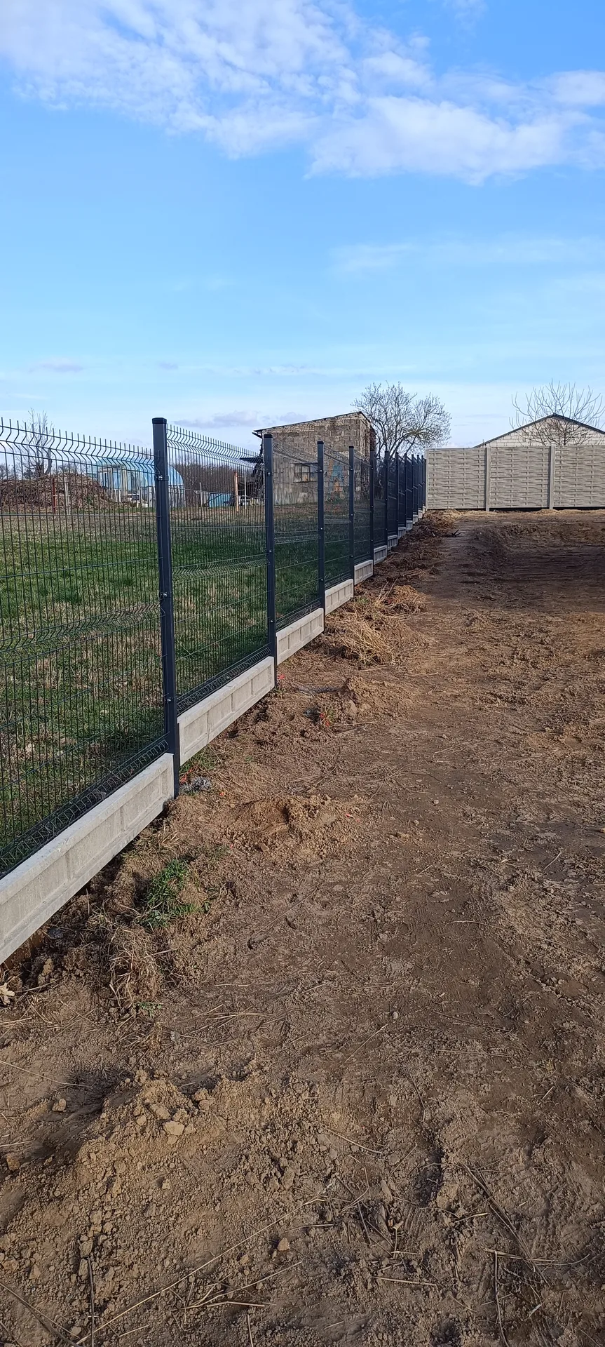 Ogrodzenie siatkowe czarne ze słupkami metalowymi i białą podmurówką betonową na terenie budowy