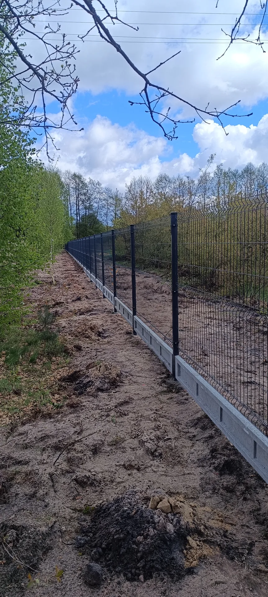 Ogrodzenie siatkowe metalowe z drewnianą podmurówką i słupkami w naturalnym otoczeniu przyleśnym