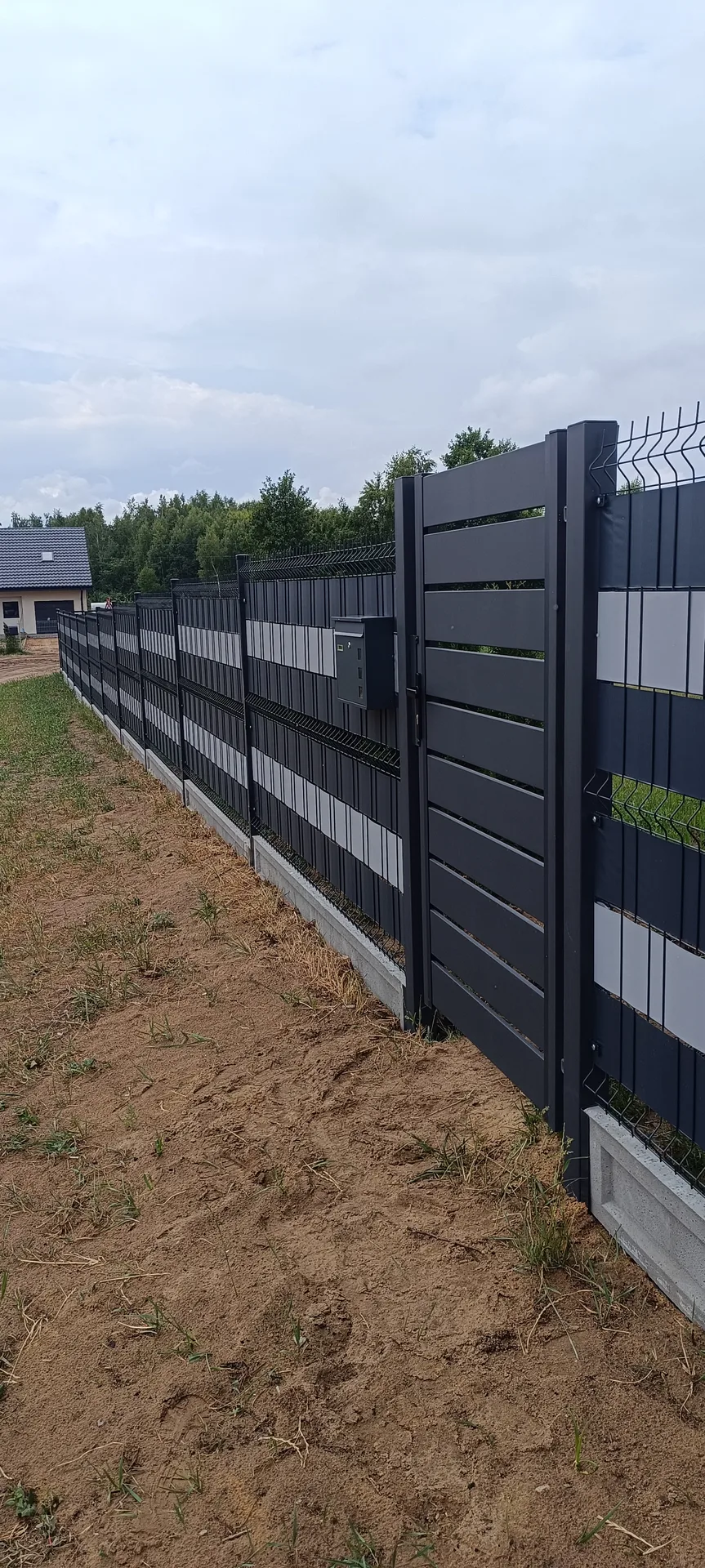 Czarne ogrodzenie panelowe z bramą wjazdową na białej podmurówce betonowej